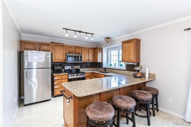 kitchen with stainless steel appliances, a sink, a peninsula, brown cabinetry, and light stone countertops