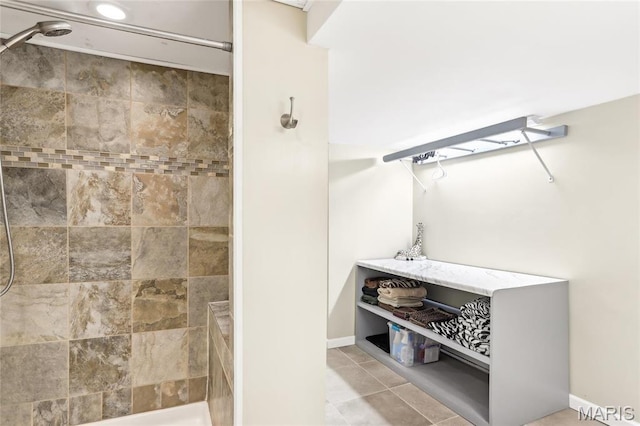 bathroom with tiled shower, baseboards, and tile patterned floors