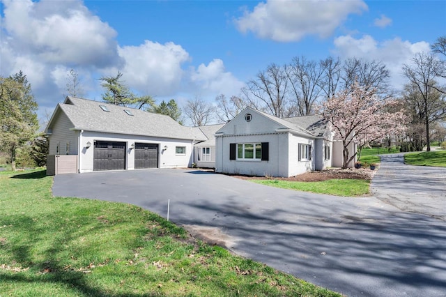 view of property exterior with a lawn, a detached garage, asphalt driveway, and a shingled roof