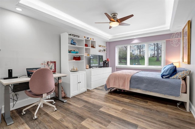 bedroom with a raised ceiling, wood finished floors, recessed lighting, a desk, and a ceiling fan