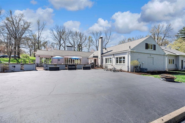 back of property with a chimney, an outdoor fire pit, and brick siding