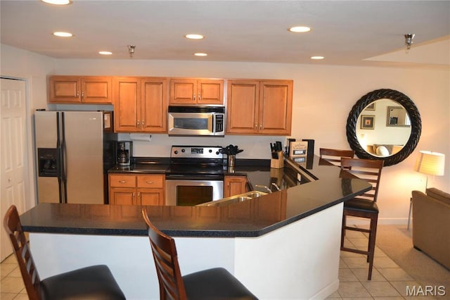 kitchen featuring appliances with stainless steel finishes, a kitchen breakfast bar, light tile patterned flooring, dark countertops, and recessed lighting