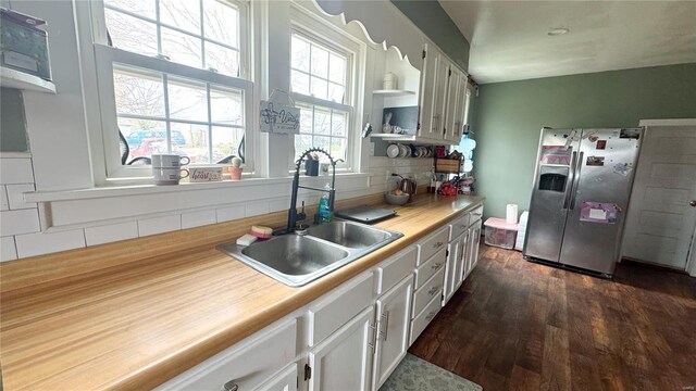 kitchen with stainless steel refrigerator with ice dispenser, a sink, dark wood finished floors, backsplash, and light countertops