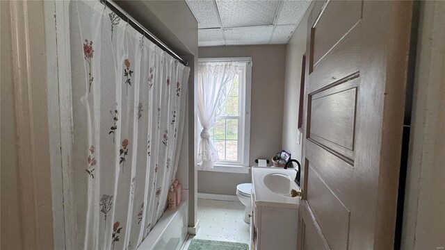 full bath featuring toilet, vanity, baseboards, and a drop ceiling