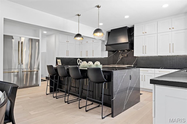 13516 Weston Park Dr, Saint Louis, MO 63131 - kitchen featuring high quality fridge, custom range hood, dark countertops, light wood-type flooring, and decorative backsplash