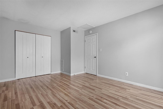 unfurnished bedroom featuring light wood-style floors, baseboards, a closet, a textured ceiling, and attic access