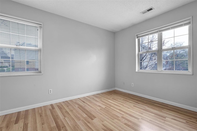 spare room featuring light wood finished floors, baseboards, and a textured ceiling
