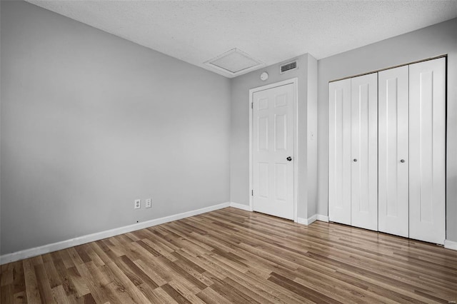 unfurnished bedroom featuring wood finished floors, baseboards, a textured ceiling, attic access, and a closet