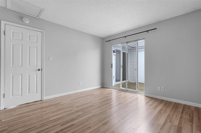 spare room featuring light wood-style floors, a textured ceiling, baseboards, and a smoke detector