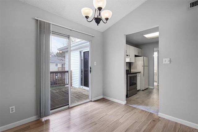 unfurnished dining area featuring a chandelier, lofted ceiling, light wood-type flooring, baseboards, and a textured ceiling