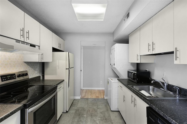 kitchen featuring black appliances, under cabinet range hood, a sink, stacked washer / dryer, and tasteful backsplash