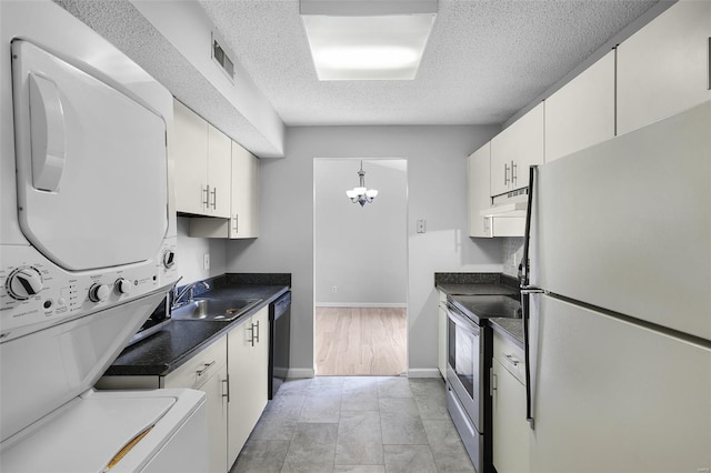 kitchen featuring freestanding refrigerator, electric range, stacked washer and clothes dryer, a sink, and a textured ceiling