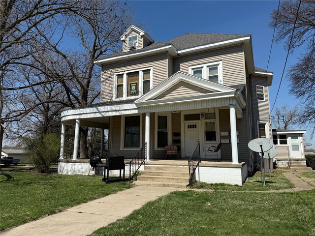 view of front facade featuring covered porch, a front lawn, and roof with shingles