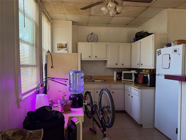 kitchen with white appliances, white cabinets, a sink, light tile patterned floors, and tasteful backsplash