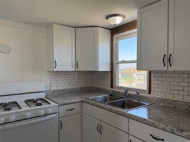 kitchen with white gas range oven, a sink, white cabinets, and backsplash