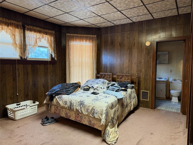 bedroom featuring light colored carpet, wooden walls, and connected bathroom