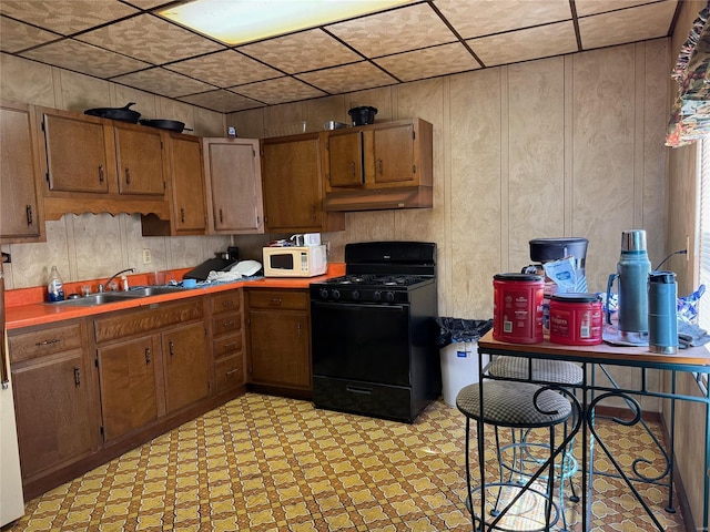 kitchen featuring black gas stove, white microwave, a sink, brown cabinetry, and under cabinet range hood