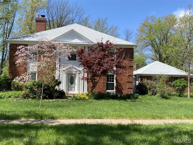 greek revival inspired property featuring a chimney, a front yard, and brick siding