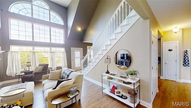 living room with wood finished floors, baseboards, stairs, plenty of natural light, and a towering ceiling