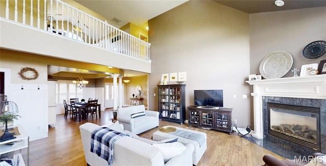living area with a chandelier, wood finished floors, a towering ceiling, and a high end fireplace