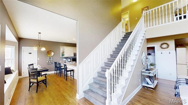 stairs with wood finished floors, baseboards, a towering ceiling, and recessed lighting