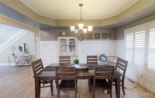 dining room with a chandelier, light wood-style flooring, crown molding, stairs, and wainscoting