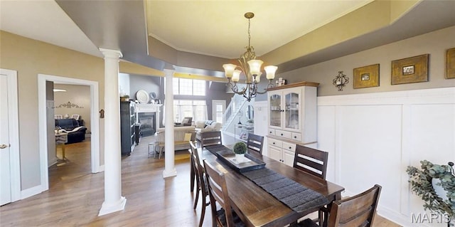 dining space featuring ornate columns, a chandelier, light wood-style flooring, a fireplace, and crown molding
