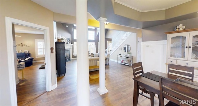dining room with ornate columns, wood finished floors, crown molding, stairway, and a fireplace