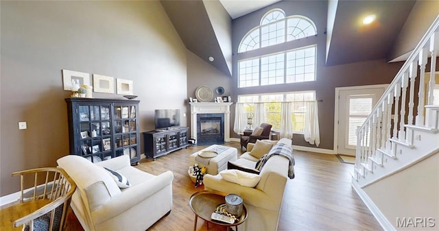 living room with a high ceiling, baseboards, stairway, a fireplace, and wood finished floors
