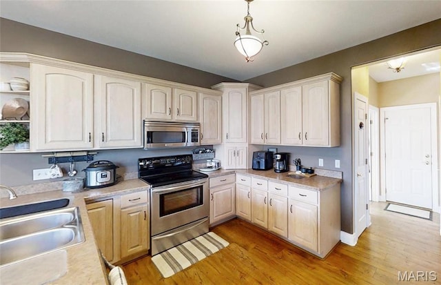 kitchen with appliances with stainless steel finishes, a sink, light wood-style flooring, light countertops, and pendant lighting