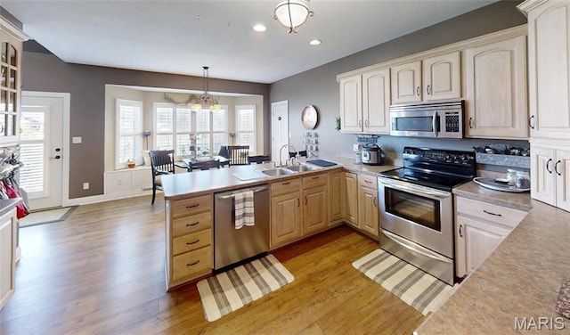 kitchen with stainless steel appliances, a sink, a peninsula, light wood-type flooring, and recessed lighting