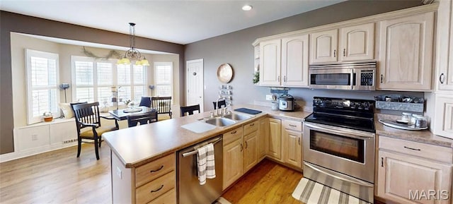 kitchen featuring appliances with stainless steel finishes, a sink, a peninsula, light wood finished floors, and a chandelier