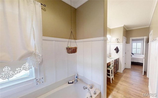 bathroom with a decorative wall, crown molding, a tub, wainscoting, and wood finished floors