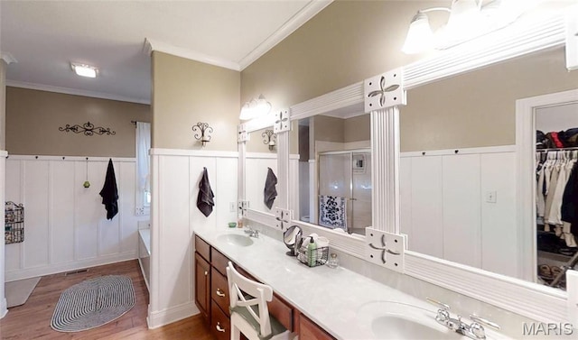 bathroom with ornamental molding, a stall shower, wood finished floors, a decorative wall, and double vanity