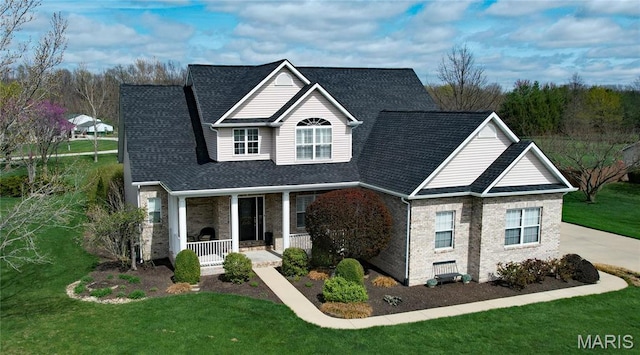 traditional-style home with covered porch, a front lawn, brick siding, and roof with shingles