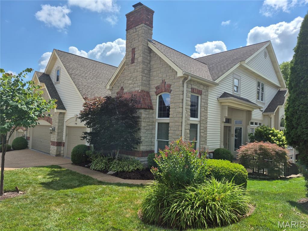 740 Stonebluff Ct, Chesterfield, MO 63005 - view of property exterior featuring stone siding, roof with shingles, driveway, a lawn, and a chimney