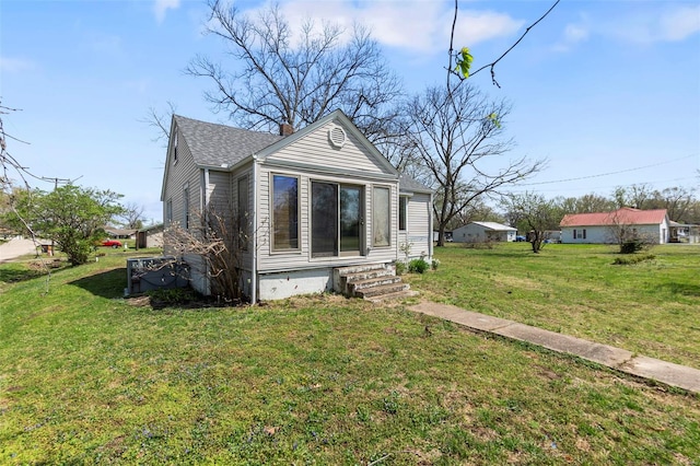 view of front of house featuring a front lawn, entry steps, roof with shingles, and a chimney