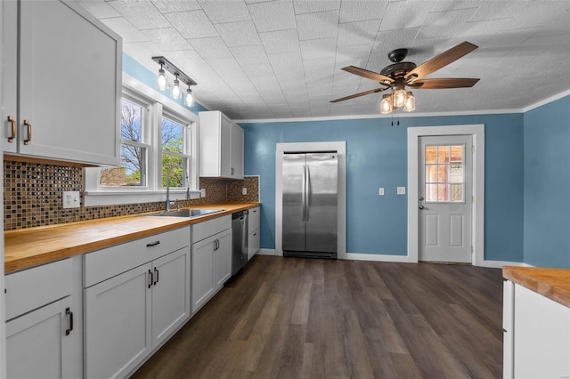 kitchen with butcher block counters, stainless steel appliances, a sink, backsplash, and dark wood-style flooring