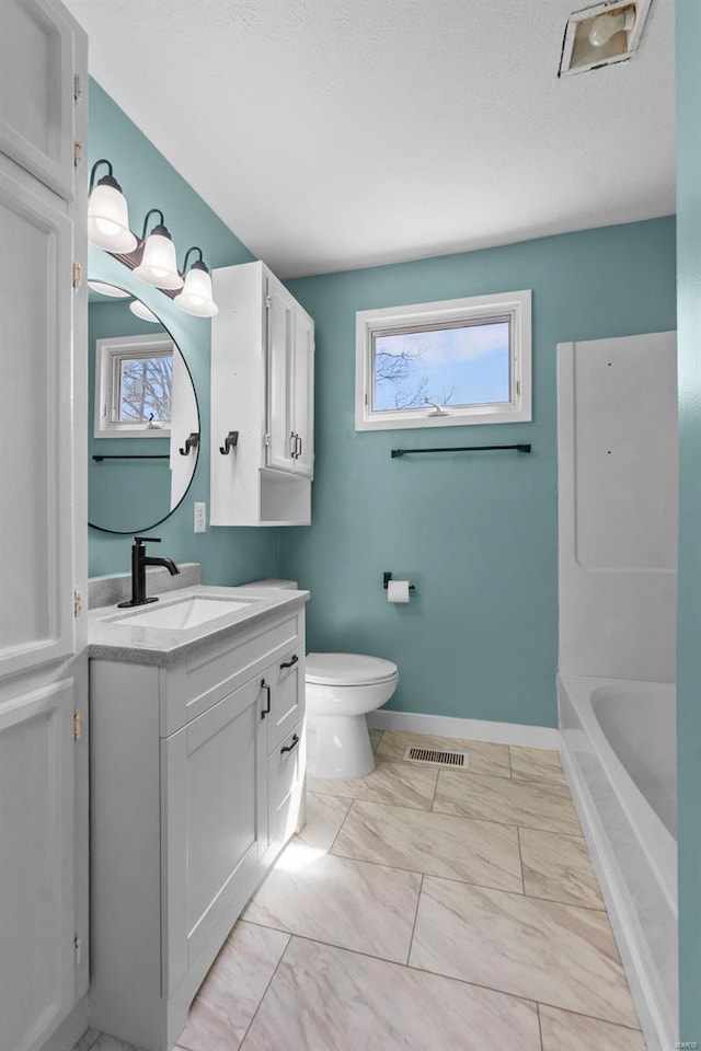 full bathroom featuring toilet, plenty of natural light, marble look tile flooring, vanity, and a textured ceiling