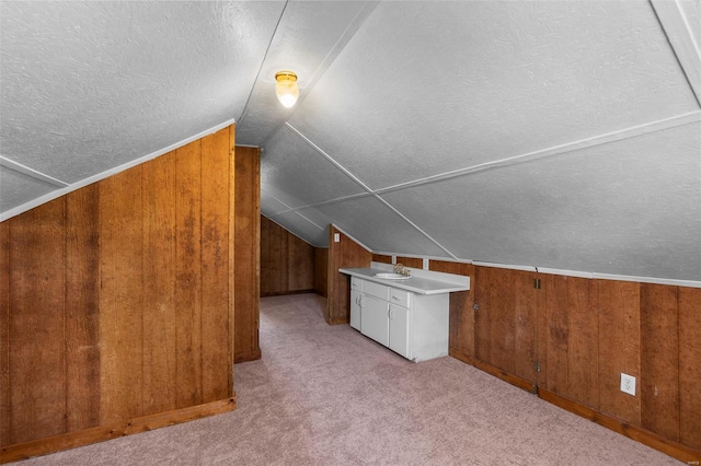 additional living space featuring wood walls, lofted ceiling, light carpet, and a textured ceiling