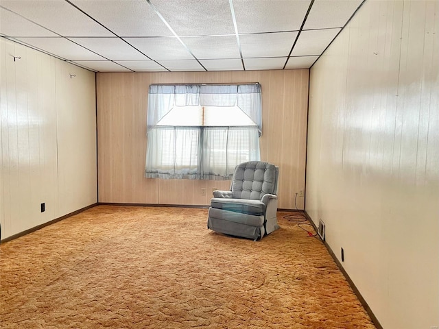 unfurnished room featuring carpet floors, wooden walls, a paneled ceiling, and baseboards