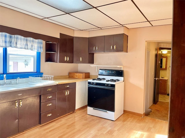 kitchen featuring white range with gas cooktop, light wood-style floors, a sink, light countertops, and a drop ceiling