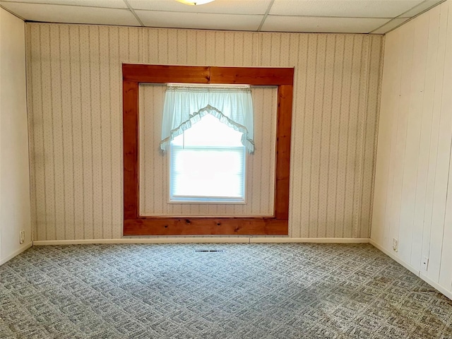 carpeted empty room with wood walls, a drop ceiling, and baseboards