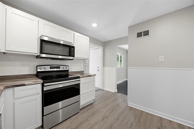 9218 Ellison Dr, Saint Louis, MO 63136 - kitchen featuring appliances with stainless steel finishes, a wainscoted wall, white cabinets, light wood-style flooring, and tasteful backsplash