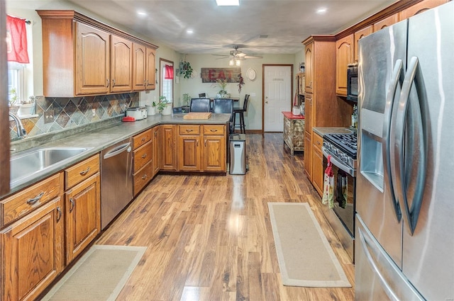 kitchen with appliances with stainless steel finishes, a peninsula, brown cabinets, ceiling fan, and a sink