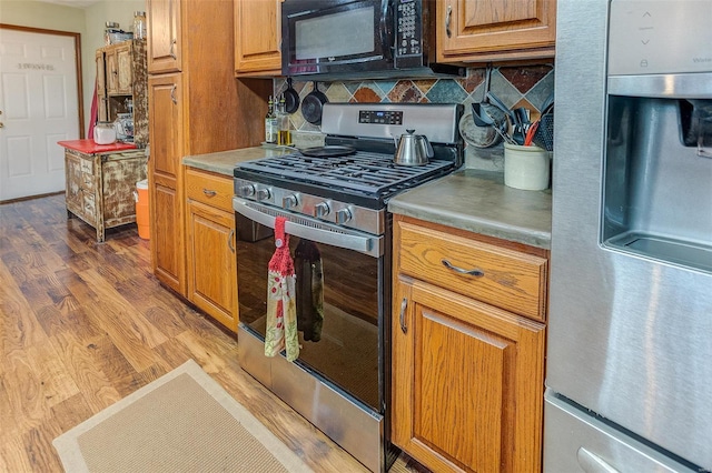 kitchen featuring appliances with stainless steel finishes, brown cabinetry, tasteful backsplash, and wood finished floors