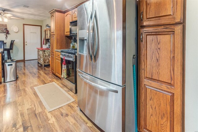 kitchen with stainless steel appliances, light wood-type flooring, a ceiling fan, and brown cabinets