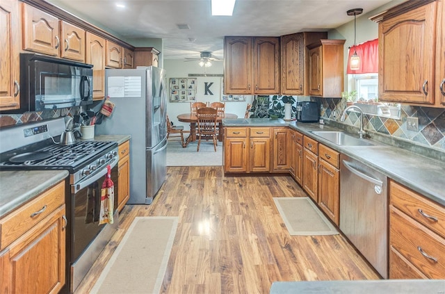 kitchen with appliances with stainless steel finishes, a sink, brown cabinetry, light wood finished floors, and a ceiling fan