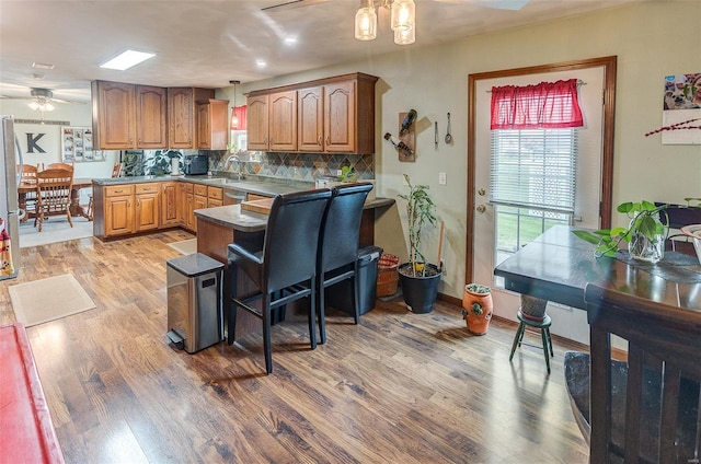 kitchen with ceiling fan, light wood-style floors, brown cabinetry, decorative backsplash, and a peninsula