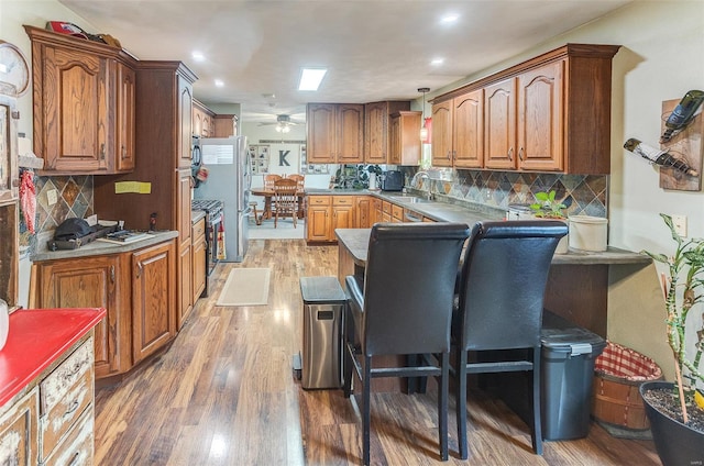 kitchen featuring a sink, light wood finished floors, a ceiling fan, stainless steel gas range oven, and decorative backsplash
